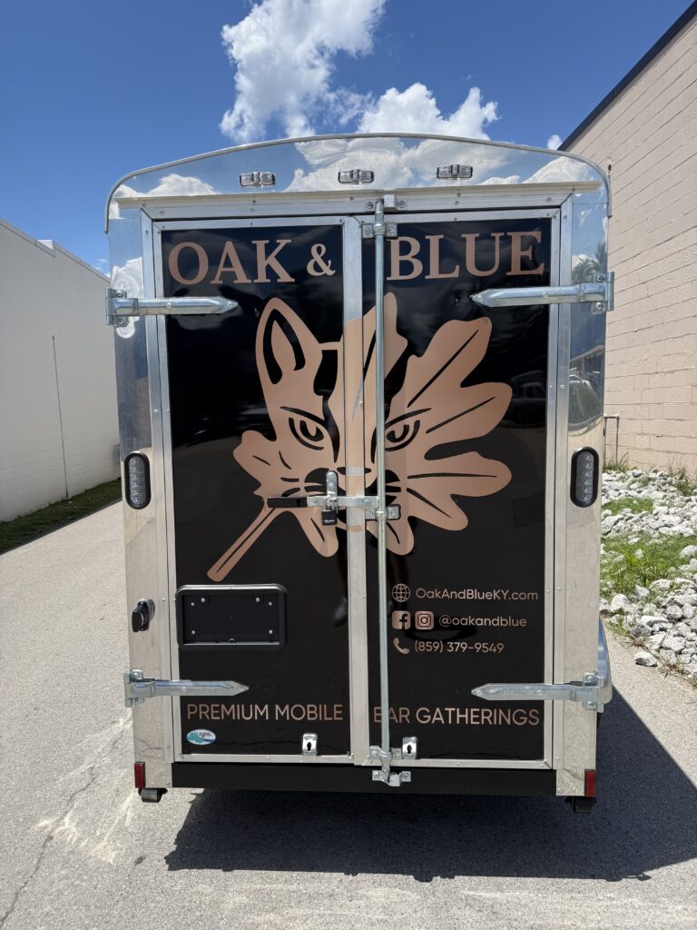 Rear view of an Oak & Blue enclosed trailer featuring a large custom logo wrap and business branding graphics.